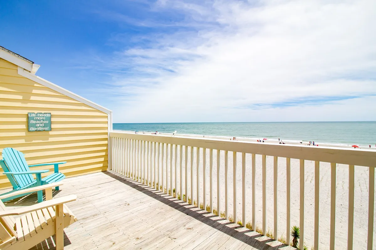 A serene exterior scene featuring blue chairs facing the ocean, a yellow house nearby, and an unobstructed beach view. The setting is peaceful and perfect for intimate moments by the shore.