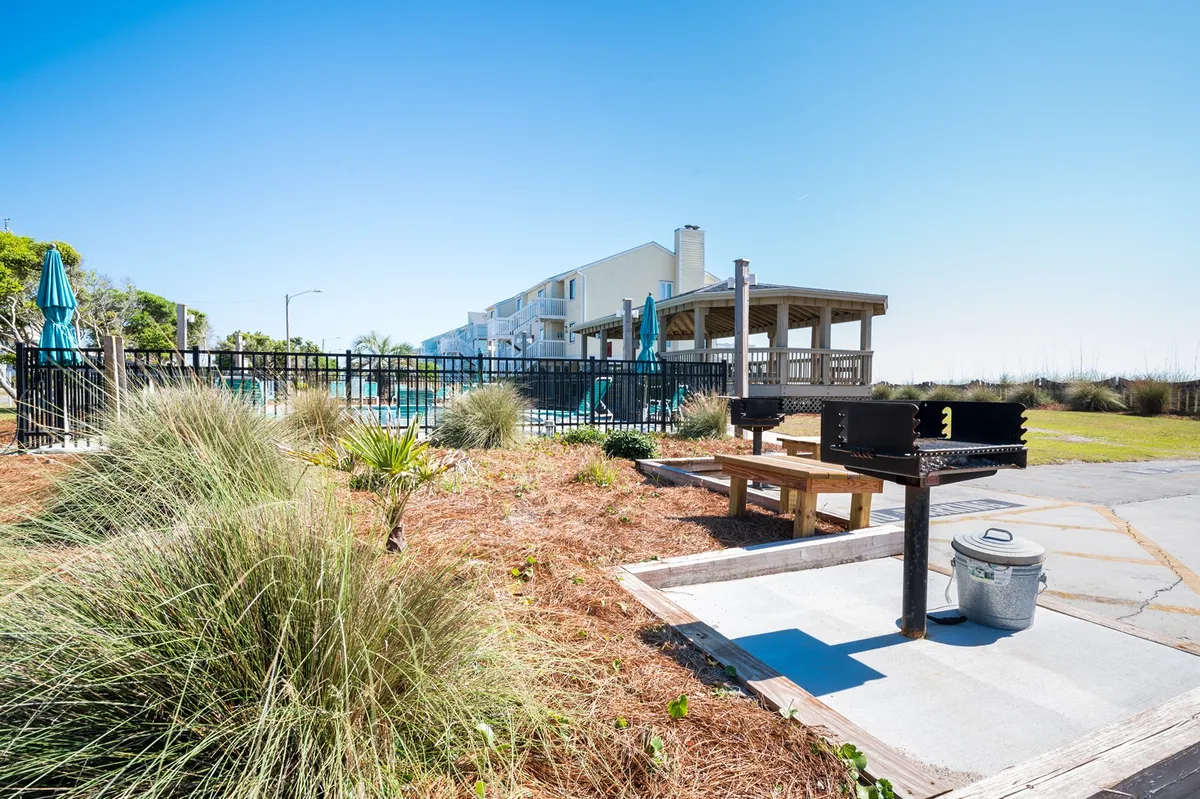 A communal grill area set beside the pool, with benches and lush greenery, providing a social, family-friendly space for outdoor meals or gatherings after beach and pool activities.