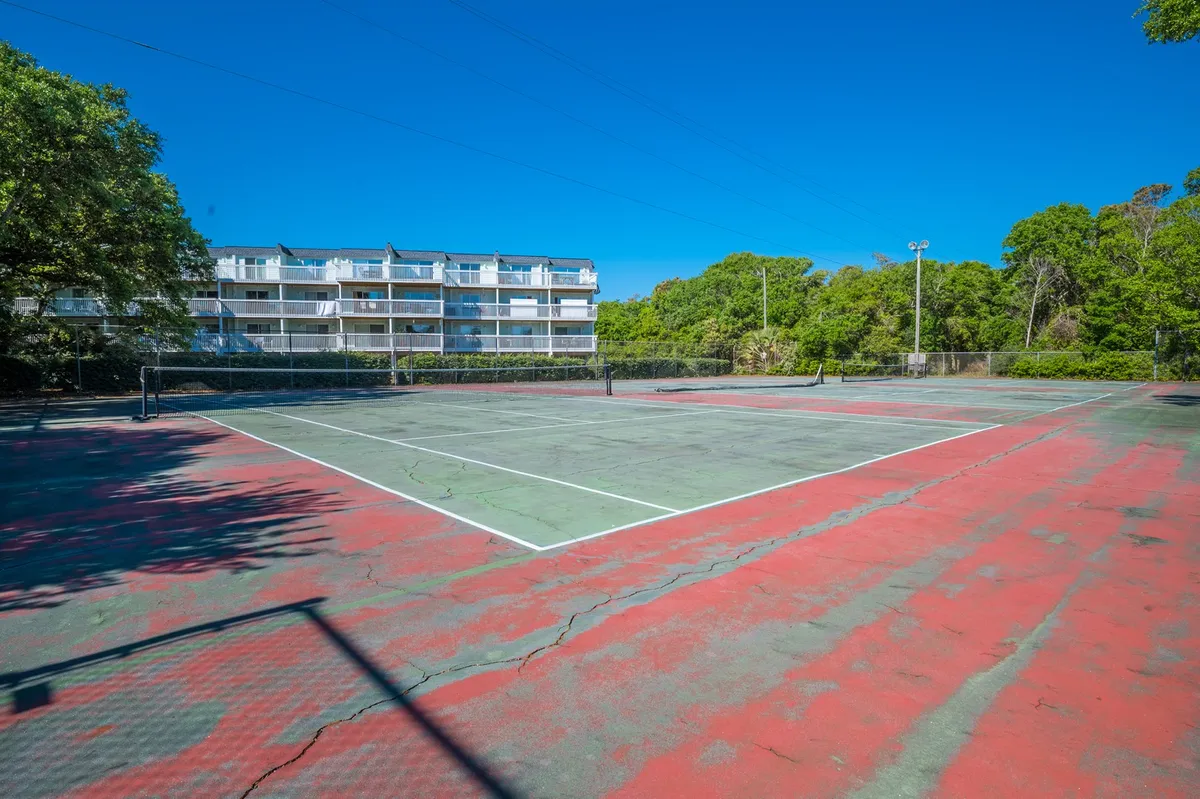A well-maintained tennis court bordered by greenery and a building in the background invites guests to play. The vibrant court lines and open space encourage active play and friendly competition among guests.