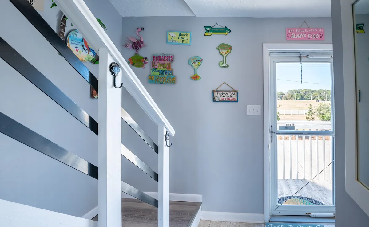 This image showcases a staircase with decorative wall signs and a doorway leading outside, highlighting the entry area. The scene exudes a welcoming, cheerful atmosphere with beach-themed decor, providing a glimpse of the transition from outside to the condo's interior.