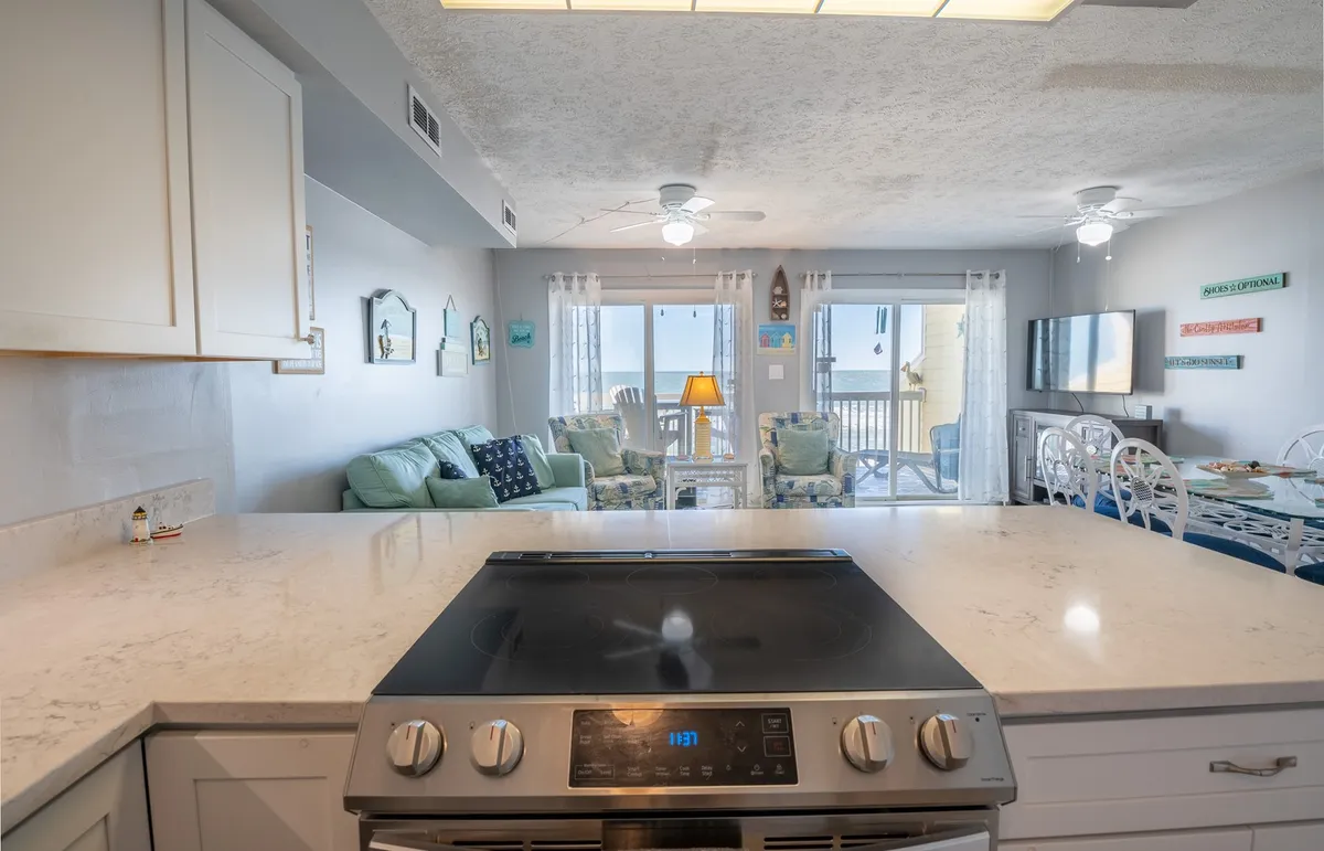 A welcoming open kitchen with a marble-topped island, stainless steel stove, and inviting seating area. Large windows lead out to a balcony, merging indoor and outdoor living and allowing plenty of light to flood the space.