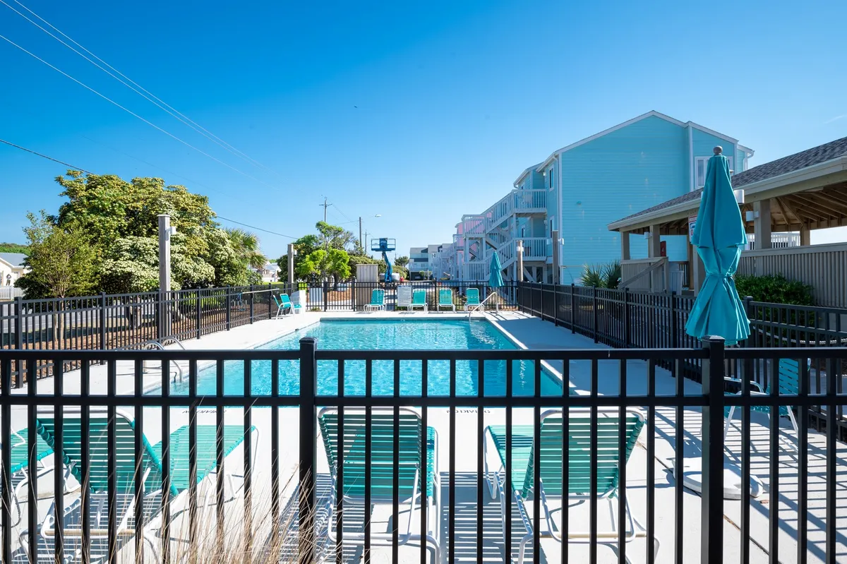A vibrant outdoor pool scene featuring a sparkling swimming pool surrounded by lounge chairs, umbrellas, and lush greenery. The area is inviting for sunbathing, swimming, and social gatherings, with ample seating for guests to relax poolside.